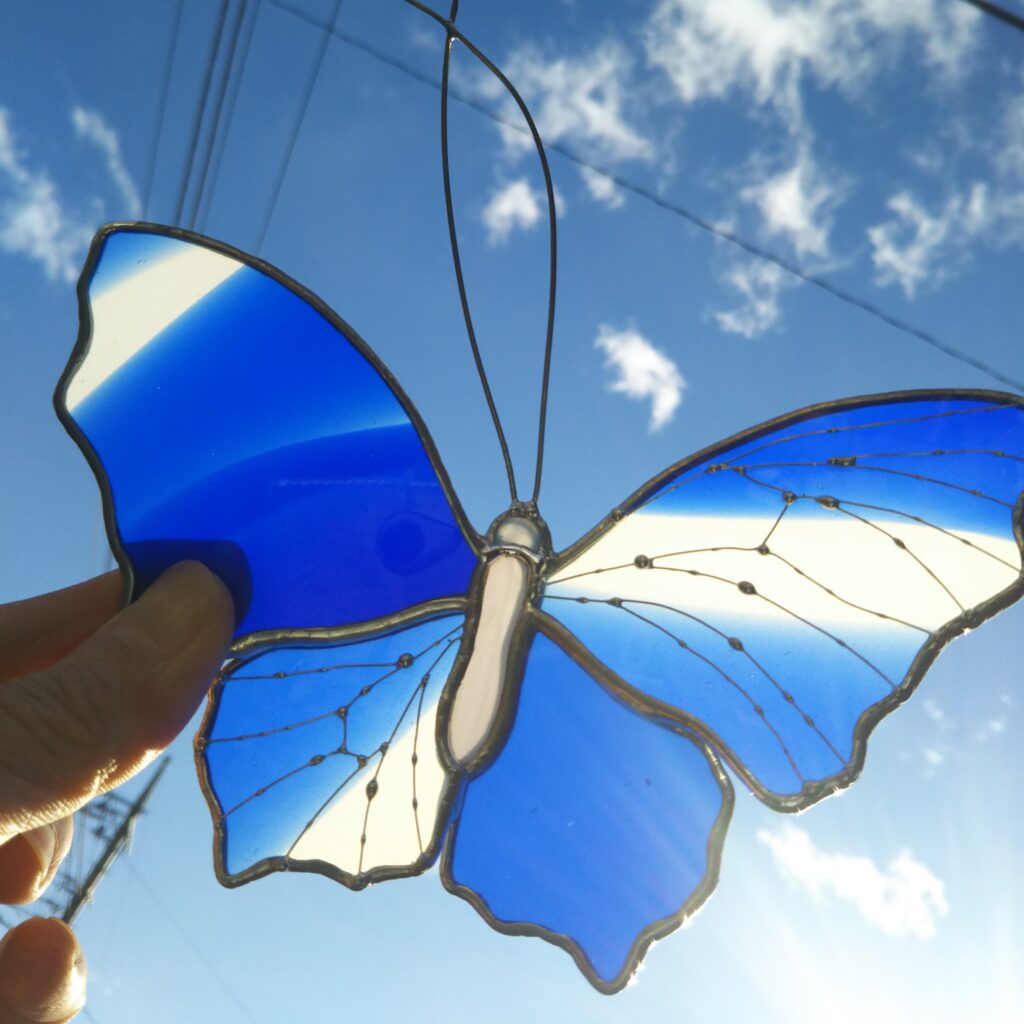 青空に蝶の形のステンドグラスをかざしています